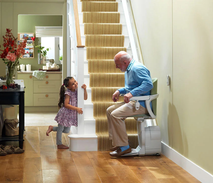 Elderly man using Stannah stairlift while granddaughter watches